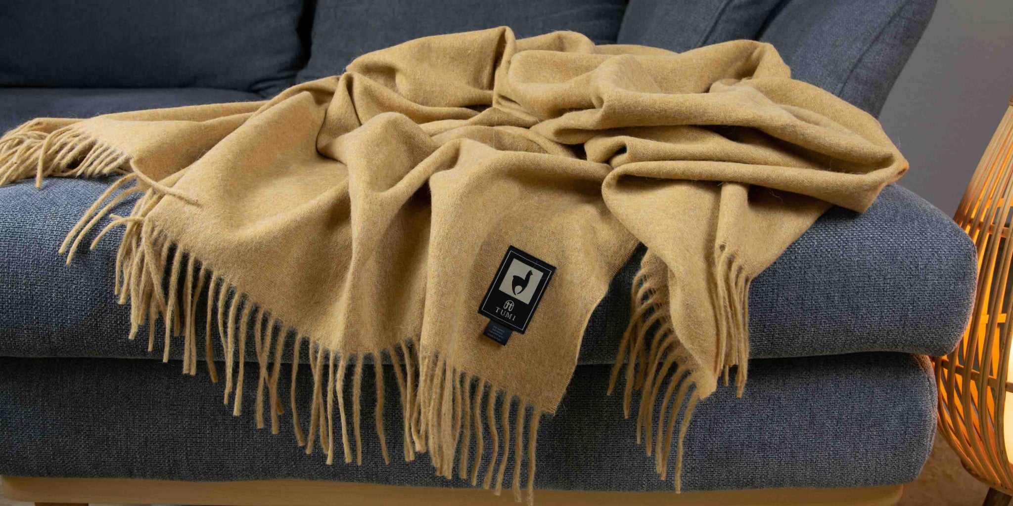 Große Alpaka Wolldecke von Alpakin in senfgelb auf einem grauen Sofa