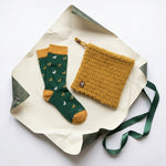 Senfgelbes Set für Alpaka Fans auf Geschenkpapier, bestehend aus grün-senfgelben Alpaka Motiv Socken und 2-in-1 Loop
