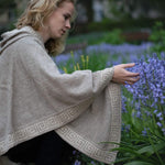 Frau mit elegantem Luz Alpaka Poncho mit Kapuze von Alpakin berührt Blumen