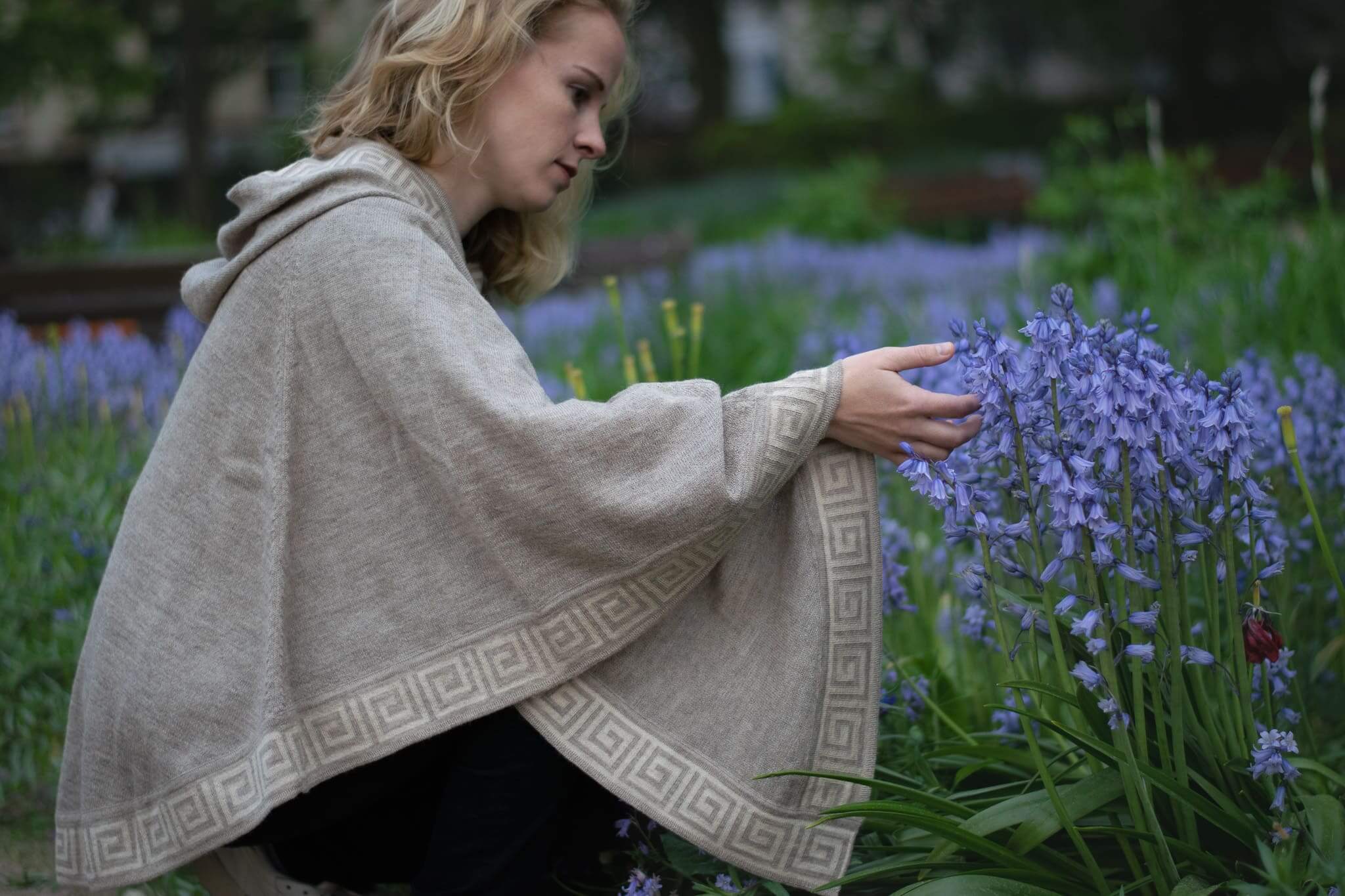 Frau mit elegantem Luz Alpaka Poncho mit Kapuze von Alpakin berührt Blumen