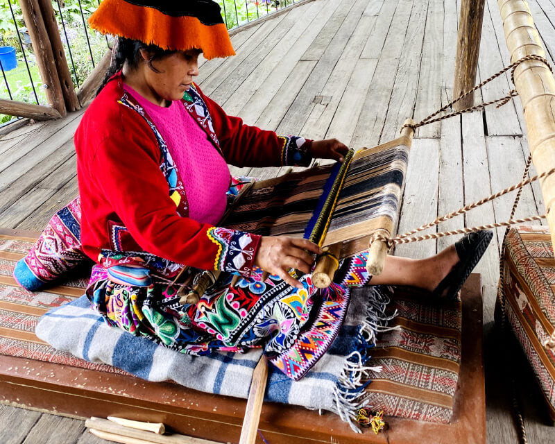Peruanerin in typisch-bunter Kleidung webt mit Alpakawolle