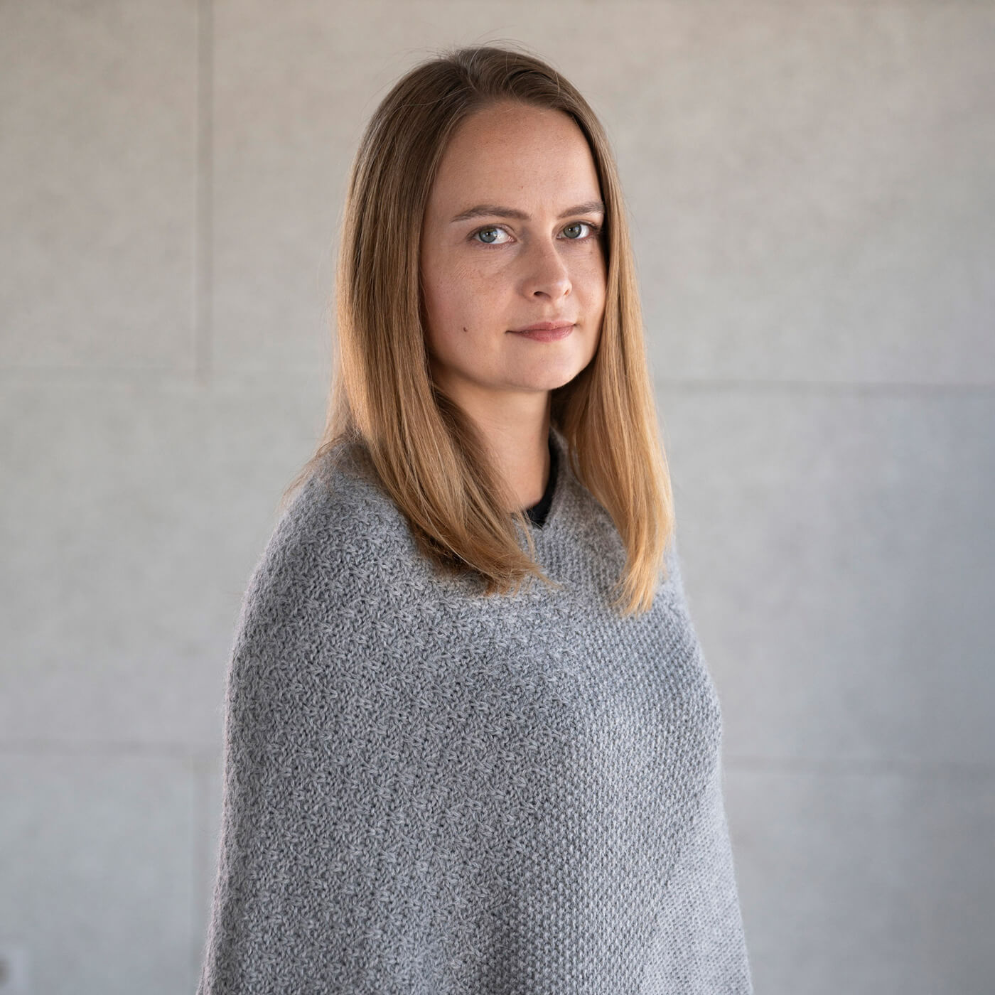 Model seitlich mit dem Naira Alpaka Strickponcho mit feinem Strickmuster in Alpaka Naturfarbe grau