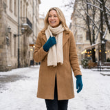 Frau trägt dunkeltürkis-farbige Alpaka Handschuhe mit Mantel und cremefarbigen Schal vor Stadtkulisse im Winter