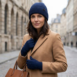 Elegante Frau mit Mantel trägt das Alpaka Winterset, bestehend aus winddichter Mütze und Handschuhe, in dunkelblau