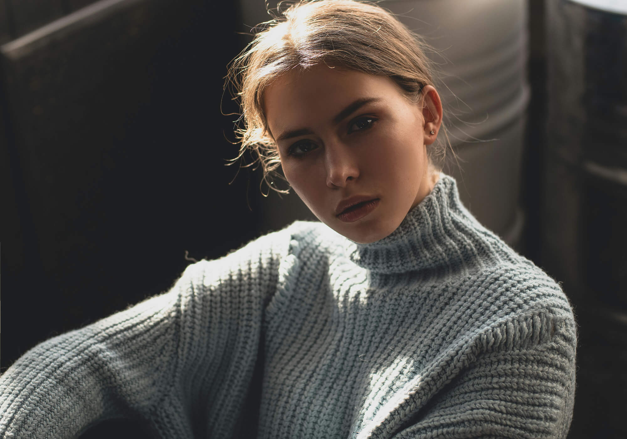 Frau mit hellblauem Grobstrick Alpaka Pullover blickt sitzend selbstbewusst in die Kamera
