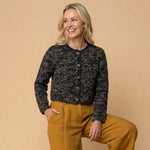 Blonde Frau kombiniert die kürzere Illari Alpaka Strickjacke mit senfgelber Leinenhose und lacht glücklich