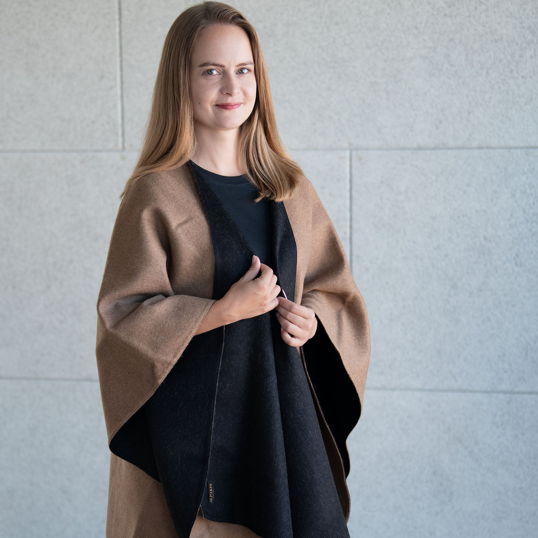 Blonde Frau trägt den Koya Alpaka Poncho Umhang in hellbraun und schwarz