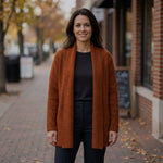 Frau trägt den warmen Alpaka Cardigan in stylischem dunkelorange vor herbstlicher Kulisse einer Stadt