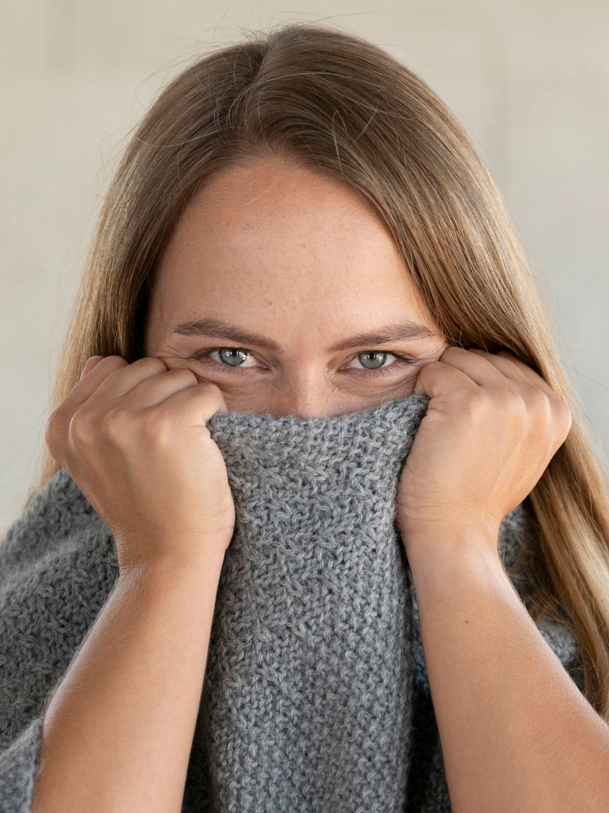 Frau kuschelt sich glücklich in ihren sanften Poncho aus Naturfaser Alpaka - Mobile Version