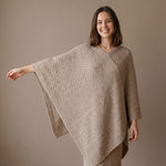 Junge Frau streckt den Arm ihres bequemen Alpaka Ponchos mit Strickmuster aus