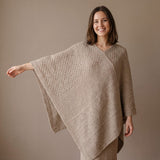 Junge Frau streckt den Arm ihres bequemen Alpaka Ponchos mit Strickmuster aus