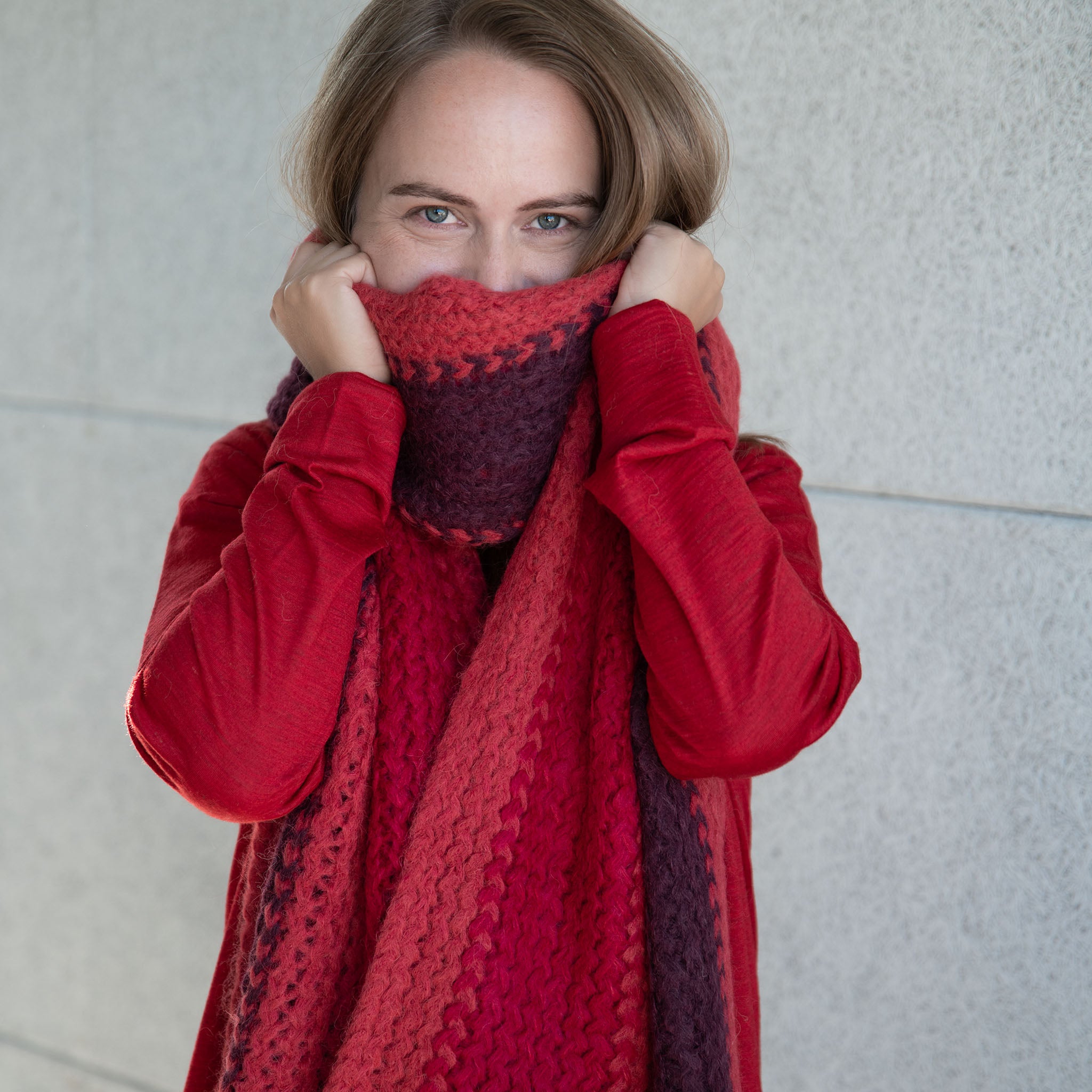 Blonde Frau bedeckt mit ihrem kuschelweichem Babyalpaka Schal in rot ihr Gesicht